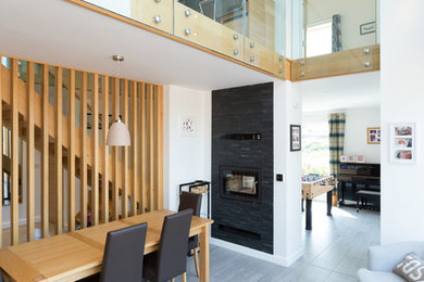 This is an example of a modern open plan dining room in West Midlands with white walls, a ribbon fireplace, a metal fireplace surround and grey floors.