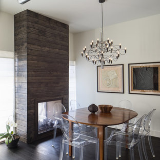 Aménagement d'une salle à manger contemporaine avec un mur blanc, un sol en bois foncé, une cheminée double-face et un manteau de cheminée en bois.