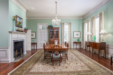 Example of a large classic medium tone wood floor enclosed dining room design in Charleston with green walls, a standard fireplace and a wood fireplace surround