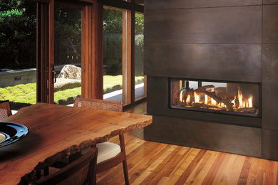 Diseño de comedor de cocina rústico de tamaño medio con paredes marrones, suelo de madera clara, chimenea de doble cara y marco de chimenea de metal