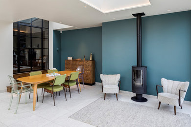 Ejemplo de comedor contemporáneo abierto con paredes azules, estufa de leña, marco de chimenea de metal y suelo gris
