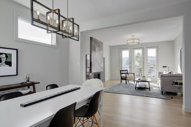 Inspiration for a contemporary open plan dining room in Calgary with grey walls, light hardwood flooring, a standard fireplace and a stone fireplace surround.