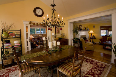 Cette image montre une salle à manger ouverte sur le salon traditionnelle avec un mur jaune, un sol en bois brun, aucune cheminée et un sol marron.