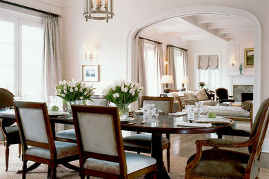 Inspiration pour une salle à manger traditionnelle avec un mur blanc, un sol en bois brun, une cheminée standard et un manteau de cheminée en pierre.