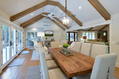 Aménagement d'une grande salle à manger ouverte sur le salon bord de mer avec un mur blanc, parquet clair, aucune cheminée, un sol marron et éclairage.