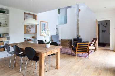 Foto di una sala da pranzo aperta verso il soggiorno design di medie dimensioni con pareti bianche, parquet chiaro, stufa a legna, cornice del camino in metallo e pavimento marrone