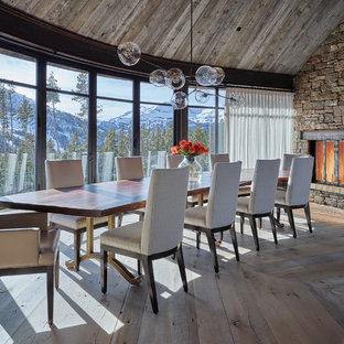 This is an example of a large country separate dining room in Other with medium hardwood floors, a standard fireplace, a stone fireplace surround and brown walls.