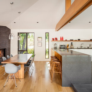 Aménagement d'une salle à manger ouverte sur le salon scandinave de taille moyenne avec un mur blanc, un sol en bois brun, une cheminée d'angle, un manteau de cheminée en brique et un sol marron.