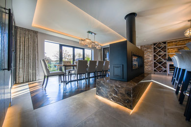 This is an example of a large contemporary kitchen/dining room in Hampshire with ceramic flooring, a two-sided fireplace, a stone fireplace surround and beige floors.