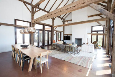 Foto de comedor de estilo de casa de campo grande abierto con paredes blancas, suelo de cemento, todas las chimeneas, suelo marrón y marco de chimenea de ladrillo