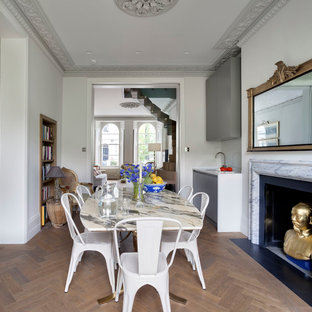 Idee per una sala da pranzo aperta verso la cucina bohémian di medie dimensioni con pareti grigie, parquet scuro, camino classico, cornice del camino in pietra e pavimento marrone