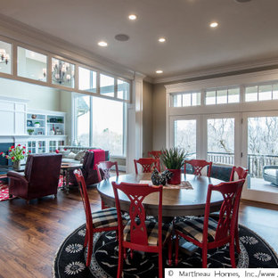 Cette image montre une grand salle à manger ouverte sur le salon traditionnelle avec un mur beige, un sol en bois brun, une cheminée standard, un manteau de cheminée en lambris de bois et un sol marron.