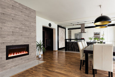 Diseño de comedor abierto con paredes blancas, suelo de madera en tonos medios, chimenea lineal y marco de chimenea de piedra