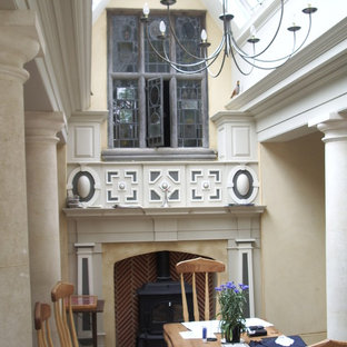 Modelo de comedor de estilo americano, de tamaño medio, con paredes beige, suelo de piedra caliza, estufa de leña y marco de chimenea de madera