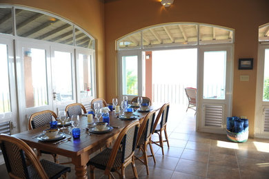 Immagine di una grande sala da pranzo aperta verso il soggiorno tropicale con pareti arancioni e pavimento in gres porcellanato
