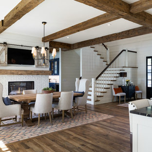 Idee per una grande sala da pranzo aperta verso la cucina costiera con pareti bianche, pavimento in legno massello medio, camino bifacciale, cornice del camino in mattoni e pavimento marrone