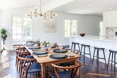 Cette image montre une grande salle à manger ouverte sur la cuisine marine avec un mur blanc, parquet foncé, un sol marron et aucune cheminée.