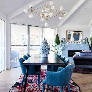 Réalisation d'une salle à manger ouverte sur le salon avec un mur blanc, un sol en bois clair, une cheminée standard et un manteau de cheminée en carrelage.