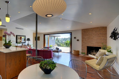 Midcentury open plan dining room in Los Angeles with a stone fireplace surround and feature lighting.