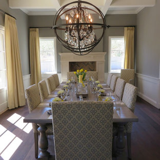 Modelo de comedor de estilo americano, grande, con paredes grises, suelo de madera en tonos medios, chimenea tradicional y marco de chimenea de madera