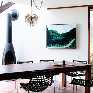 Inspiration pour une salle à manger bohème fermée et de taille moyenne avec un sol en brique, un poêle à bois, un mur blanc et un manteau de cheminée en métal.