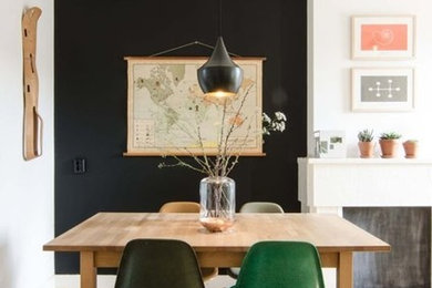 Пример оригинального дизайна: кухня-столовая в стиле фьюжн с черными стенами, светлым паркетным полом, стандартным камином и фасадом камина из дерева