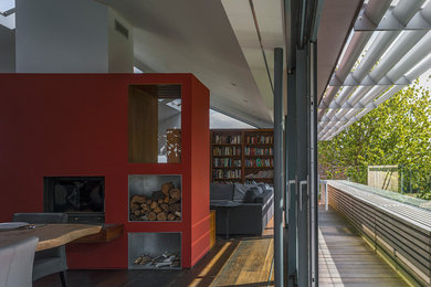Imagen de comedor contemporáneo grande abierto con paredes rojas, suelo de madera oscura, estufa de leña, marco de chimenea de yeso y suelo marrón