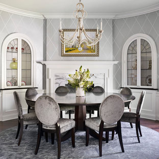 Immagine di una sala da pranzo classica con pareti grigie, parquet scuro, cornice del camino in pietra e camino classico