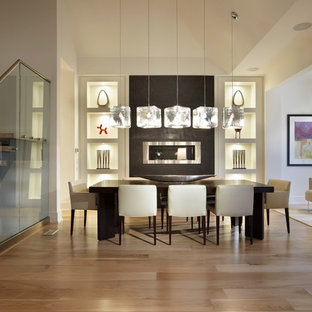 Esempio di una sala da pranzo aperta verso il soggiorno minimalista di medie dimensioni con pareti bianche, parquet chiaro, camino lineare Ribbon e cornice del camino in cemento