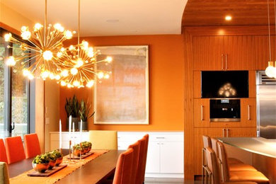 Immagine di un'ampia sala da pranzo aperta verso la cucina moderna con pareti arancioni, pavimento in sughero, camino sospeso, cornice del camino in legno e pavimento grigio