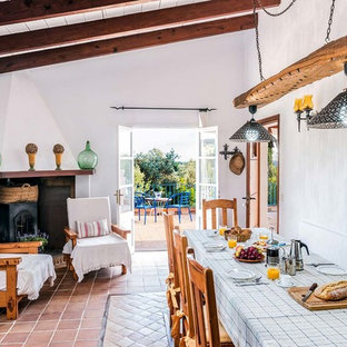 Foto di una sala da pranzo aperta verso il soggiorno mediterranea con pareti bianche, pavimento in terracotta e stufa a legna