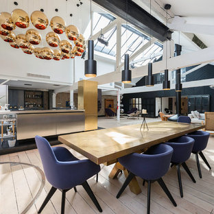Cette photo montre une grand salle à manger ouverte sur le salon industrielle avec un mur blanc, un sol en bois clair, cheminée suspendue et un manteau de cheminée en métal.