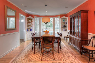 Immagine di una grande sala da pranzo aperta verso la cucina classica con pareti arancioni e pavimento in legno massello medio