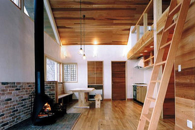 Modelo de comedor contemporáneo abierto con paredes blancas, suelo de madera clara, estufa de leña y marco de chimenea de ladrillo