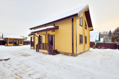 На фото: маленький, двухэтажный, деревянный, желтый частный загородный дом в классическом стиле с двускатной крышей и крышей из гибкой черепицы для на участке и в саду