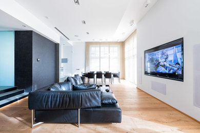 Foto di un grande home theatre minimal aperto con pareti bianche, pavimento in legno verniciato e TV a parete