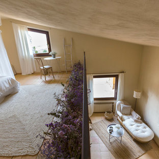 Ejemplo de dormitorio tipo loft, campestre, grande, sin chimenea, con paredes beige y suelo de baldosas de terracota