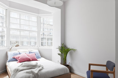 Modelo de dormitorio contemporáneo sin chimenea con suelo de madera en tonos medios y paredes blancas