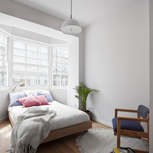 Modelo de dormitorio contemporáneo, sin chimenea, con suelo de madera en tonos medios y paredes blancas