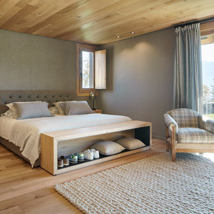 Modelo de dormitorio principal, de estilo de casa de campo, grande, con suelo de madera clara, paredes grises y suelo marrón