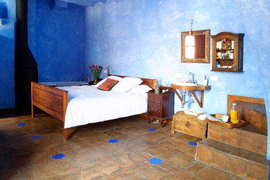 Ejemplo de dormitorio principal rural grande sin chimenea con paredes azules y suelo de baldosas de terracota