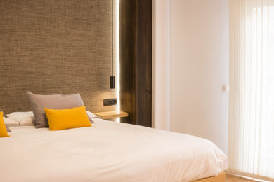 Contemporary master bedroom in Valencia with white walls, laminate floors and panelled walls.