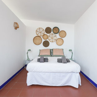 Imagen de dormitorio tipo loft, costero, de tamaño medio, sin chimenea, con paredes blancas, suelo de baldosas de terracota y suelo rojo