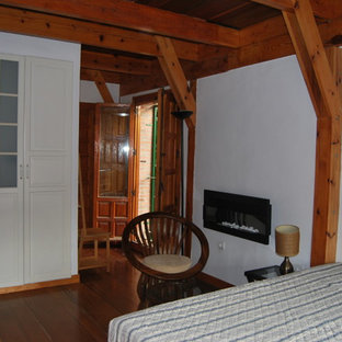 Foto de habitación de invitados campestre, grande, con paredes blancas, suelo de madera en tonos medios, chimenea lineal y marco de chimenea de metal