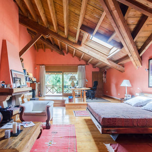 Diseño de dormitorio principal, rural, grande, con paredes rojas, suelo de madera en tonos medios, chimenea tradicional y marco de chimenea de piedra