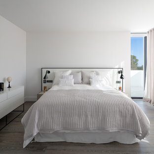 Modelo de dormitorio principal, contemporáneo, con paredes blancas, suelo de madera en tonos medios y suelo marrón