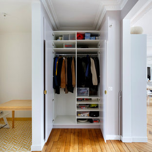 Idées déco pour un petit placard dressing contemporain neutre avec des portes de placard blanches et un sol en bois brun.