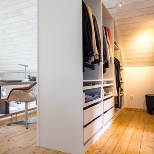 Cette image montre un dressing room design neutre avec un placard à porte plane, des portes de placard blanches et un sol en bois clair.