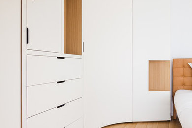 Diseño de armario unisex actual grande con armarios con rebordes decorativos, puertas de armario blancas, suelo de madera clara y suelo beige