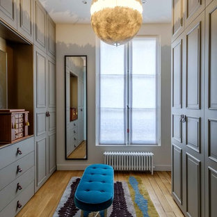 Cette image montre un grand dressing room traditionnel pour une femme avec un placard avec porte à panneau surélevé, des portes de placard grises et un sol en bois clair.